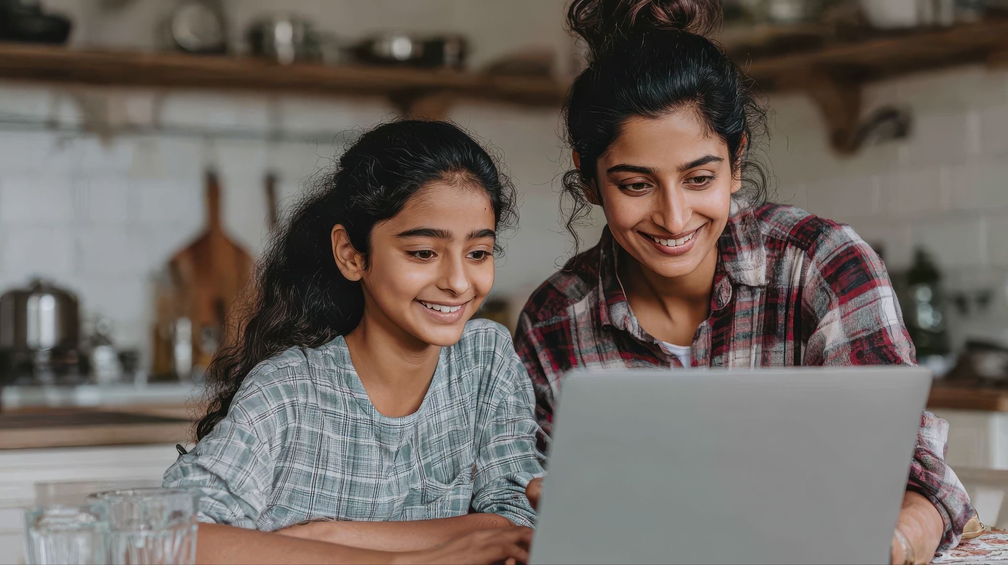 Two smiling people, an adult and a child, look at a laptop.