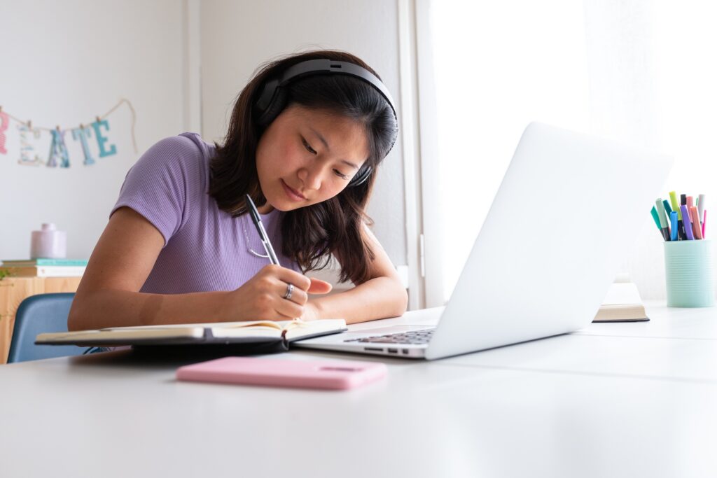 A high school student learning at home with a laptop and notepad